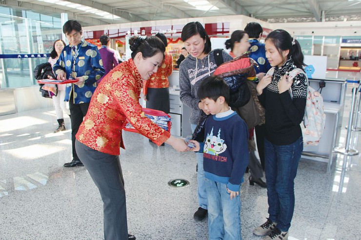 中国民族衣装姿のスタッフから記念品を受け取る乗客